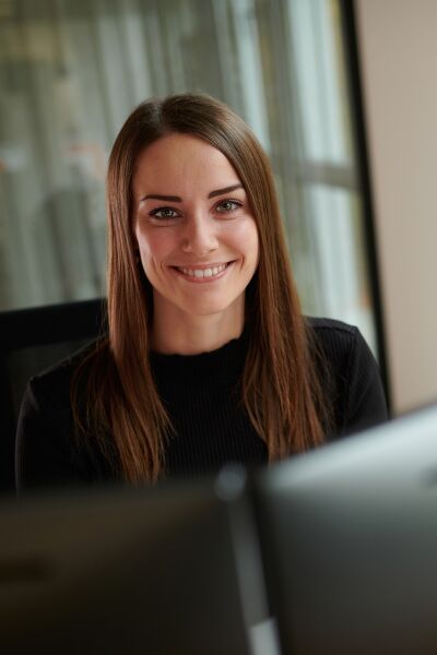 A woman sits at her desk, smiling warmly into the camera.