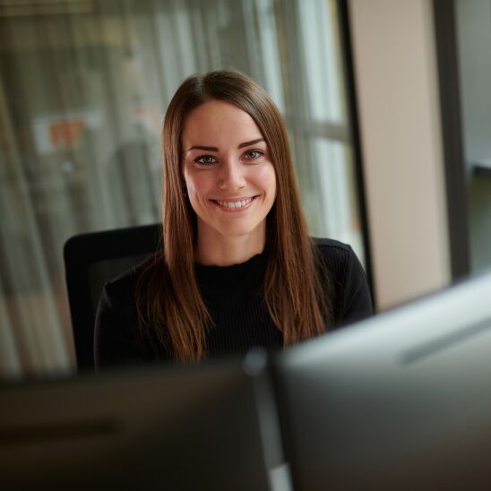 Female SIXT employee sitting at desk smiling at camera in office