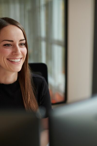 A woman sits at her desk, smiling warmly as she engages with her work.