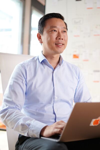 A man is sitting in front of a wall in the SIXT office filled with notes, looking thoughtful yet smiling as he engages with his computer.