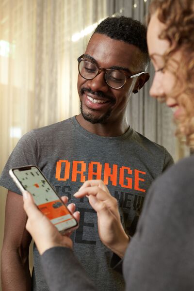 A woman is holding a smartphone in her hand, showing something to a man beside her, and both are smiling.