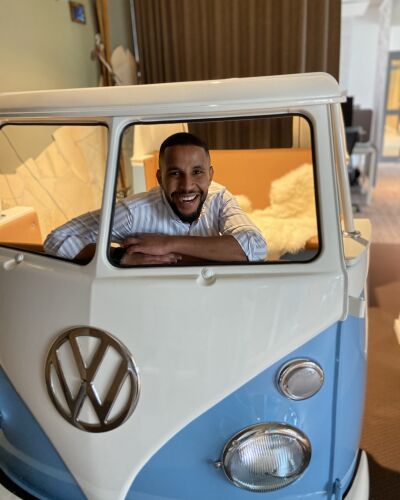 Yussuf is sitting and laughing in an old, disassembled VW bus that is in his office.