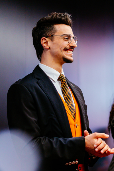 Smiling SIXT sales consultant behind the counter in a branch, wearing the company uniform with a black and orange tie.