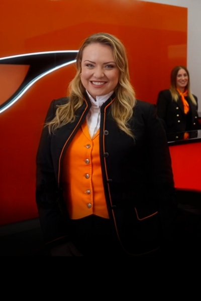 Lia, a smiling Rental Sales Agent in her SIXT uniform, standing in front of the counter at a SIXT branch.