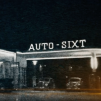 A black-and-white photo of a SIXT branch with vintage cars parked underneath the sign "Auto - SIXT" above the storefront.