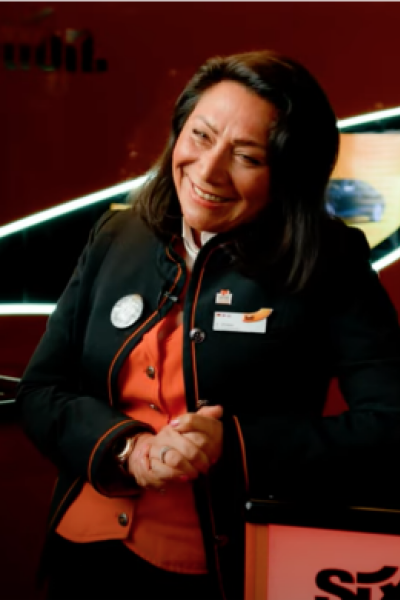 A Rental Sales Agent in her SIXT uniform stands smiling in a SIXT branch.