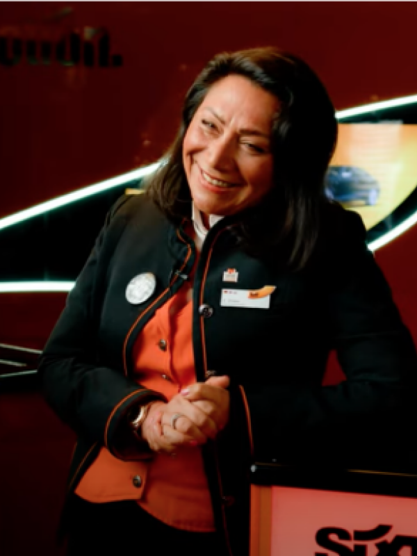 A Rental Sales Agent in her SIXT uniform stands smiling in a SIXT branch.