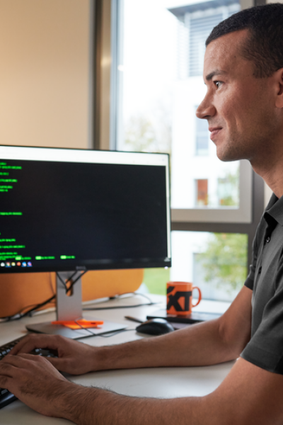 A man sits at his desk, typing on his keyboard and looking at his screen, with the SIXT logo is visible in the background.