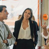 A group of people are having a conversation, listening to each other with interest. Sixt-branded orange balloons can be seen in the background, adding a festive touch.