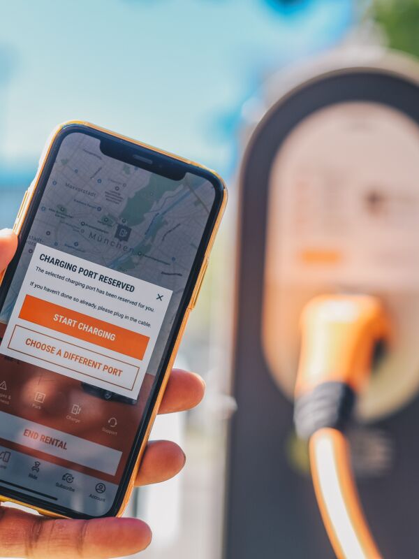 A close-up using the SIXT mobile app to reserve a charging port at an electric vehicle charging station, illustrating the infrastructure.