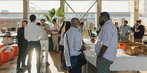 Many people are talking to each other in small groups, with a large table filled with food and drinks, and SIXT balloons decorating the scene.