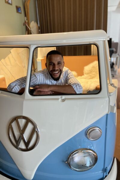 Yussuf is sitting and laughing in an old, disassembled VW bus that is in his office.