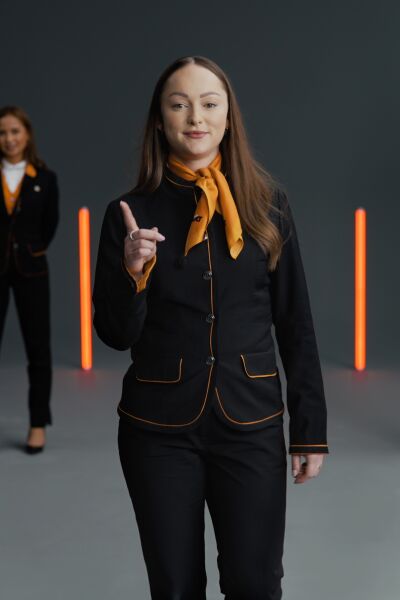 A person in a Sixt uniform in the foreground is raising their index finger. In the background, several people can be seen, and the image is illuminated by orange-colored light beams.