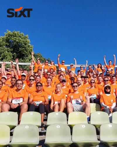 A group of people wearing orange sport-shirts with numbers on them are sitting on bleachers, smiling together.