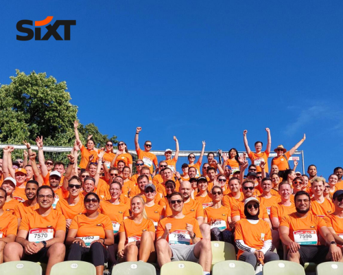 A group of people wearing orange sport-shirts with numbers on them are sitting on bleachers, smiling together.