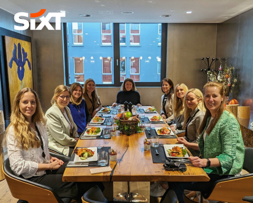A group of women sitting together at a dining table, smiling, with food in front of them.