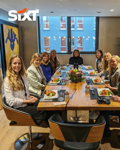A group of women sitting together at a dining table, smiling, with food in front of them.