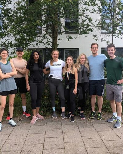 A group of people standing outdoors in sportswear, smiling in front of trees.