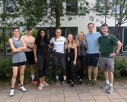 A group of people standing outdoors in sportswear, smiling in front of trees.