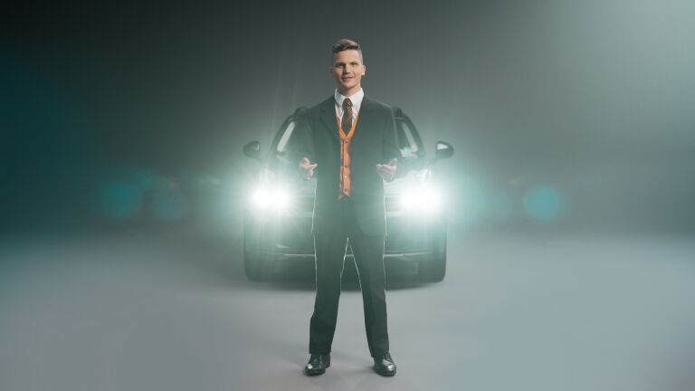 A man standing in front of a car with its headlights on.