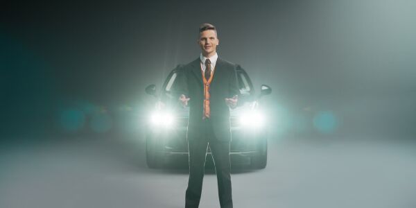 A man standing in front of a car with its headlights on.