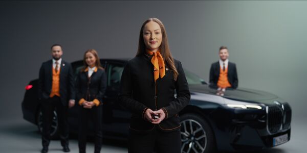 In the foreground, a woman dressed in the SIXT uniform holds a set of car keys, while in the background, a BMW is visible along with three other Sixt employees.