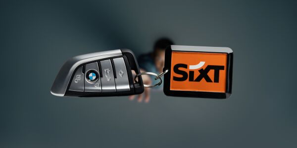 In the foreground, a BMW car key with a SIXT keychain, while in the background, a man throws the key into the air.