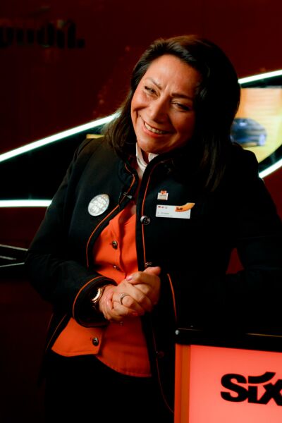 A Rental Sales Agent in her SIXT uniform stands smiling in a SIXT branch.