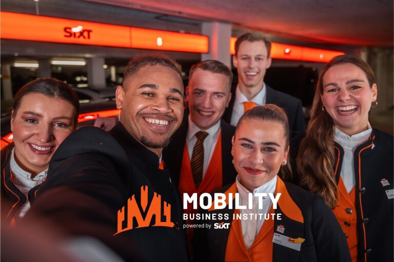 A group of smiling rental sales agents in professional uniforms stands in front of a SIXT rental location, representing the Mobility Business Institute and showcasing SIXT’s commitment to customer service and professional training in the car rental industry.